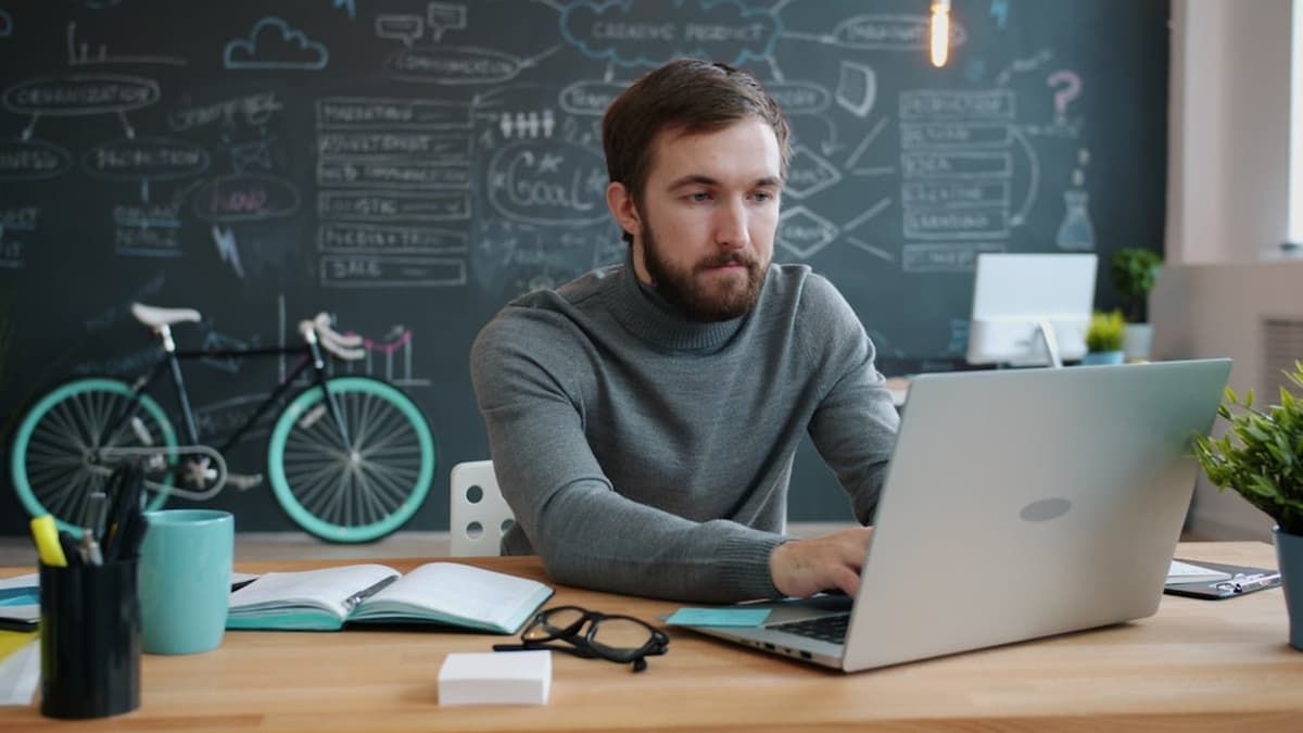 A freelancer working on a laptop at a desk in front of a chalkboard full of ideas.