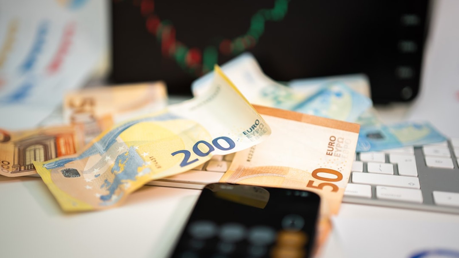 Euro banknotes and a calculator on a desk in front of a rising chart.