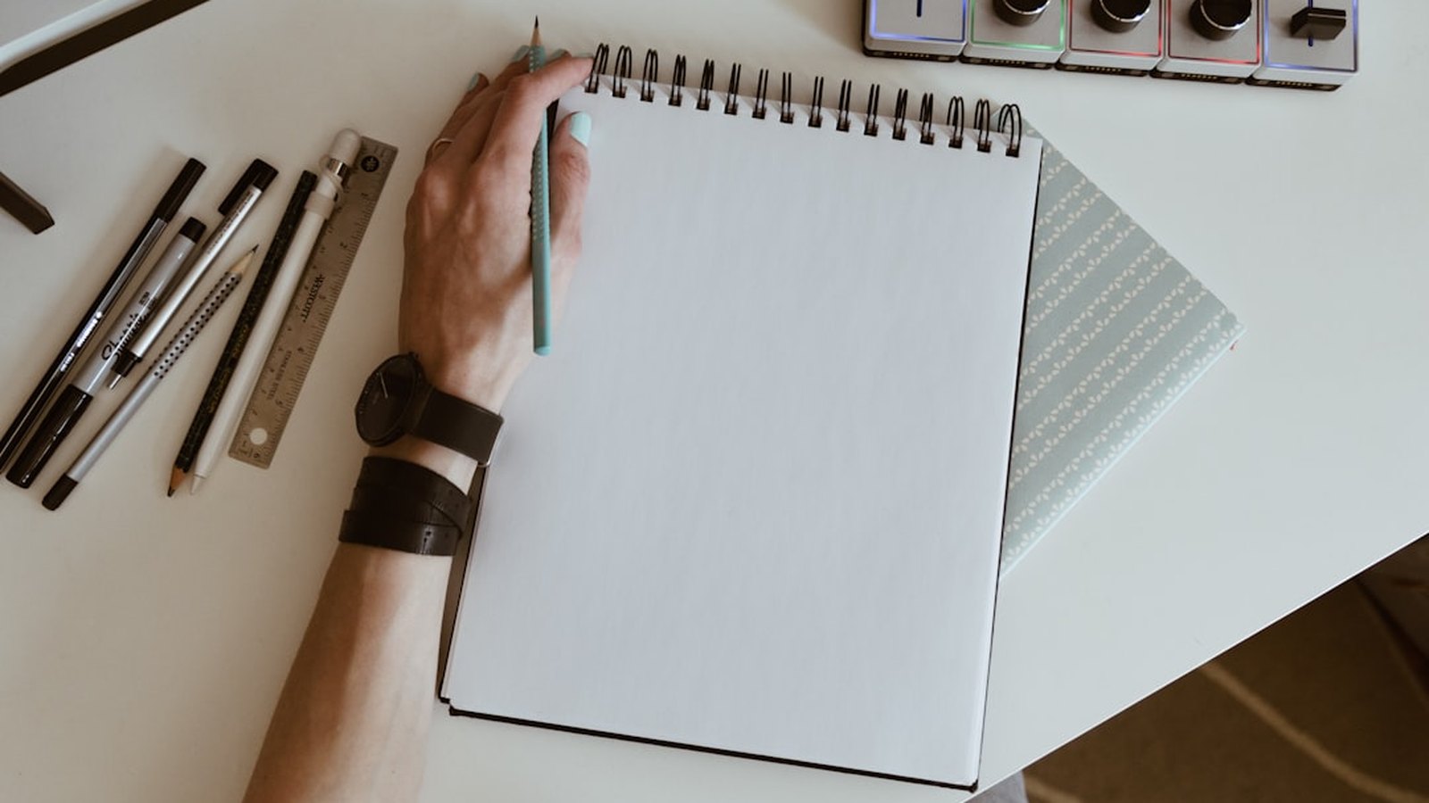 A hand sketching in a blank notebook surrounded by pens and rulers, planning a freelance skill.